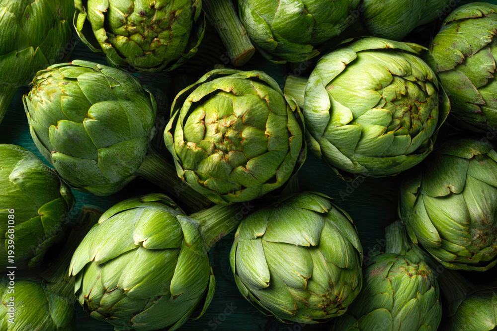 Obraz premium Fresh green artichokes arranged closely on a dark wooden surface, showcasing their unique textures and shapes, ideal for culinary or agricultural themes