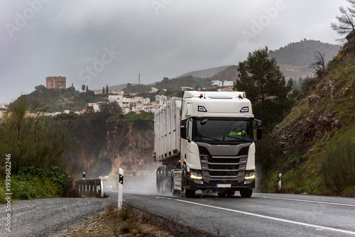 Recycling container truck driving on a rain soaked road near a village