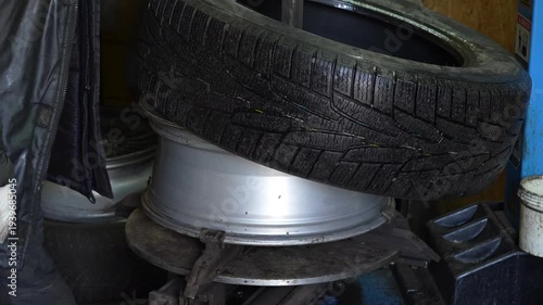 Auto mechanic removing a car tire from wheel rim using professional tire changing machine in garage workshop. Automotive repair, vehicle maintenance and tire replacement process.