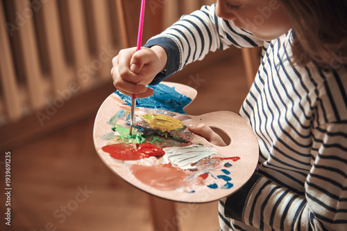 Child mixing colors on palette with paint brush