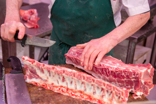 A butcher cuts a piece of pork carcass with a large knife.