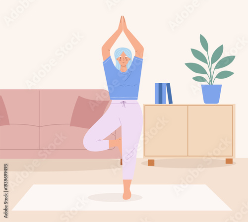 Active senior woman practicing yoga. Elderly female in tree pose in a cozy living room. Interior background for aging, wellness, health and active lifestyle design.