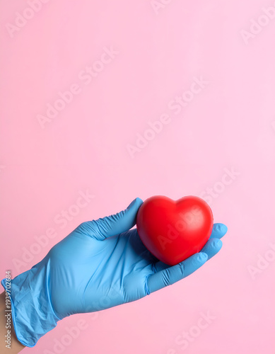 Gloved hand holds red heart against pink background