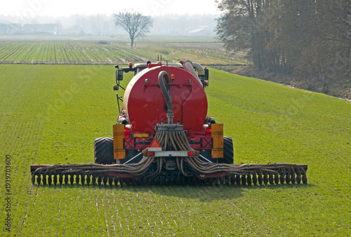 Tractor with red slurry tank fertilizing grassland