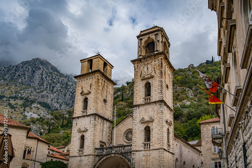 Historic towers stand tall in Kotor, Montenegro under a cloudy sky surrounded by mountains in early evening light