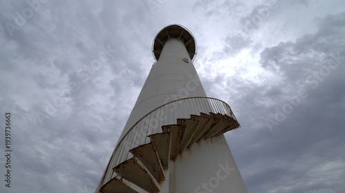 White lighthouse with spiral staircase against cloudy sky