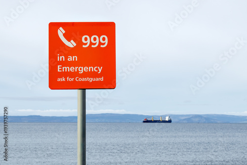 Photos Emergency 999 coastguard sign at coast with cargo ship in background