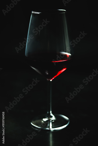 Red wine in elegant glass on dark background creating moody atmosphere, reflecting light and shadow, featuring luxury beverage