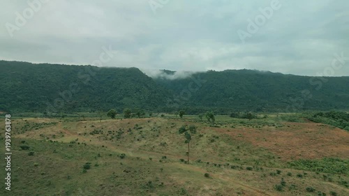 Cinematic drone aerial view of a winding road through lush tea gardens and forest hills in Jaflong, Sylhet, Bangladesh. Peaceful countryside landscape with clouds gathering