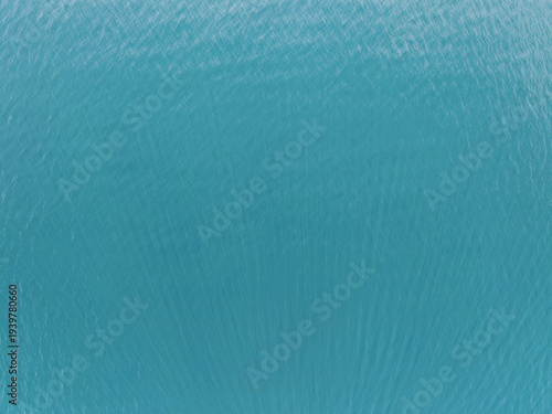 Stunning aerial top down view of vibrant turquoise sea water surface with organic ripple patterns, perfect for summer background.