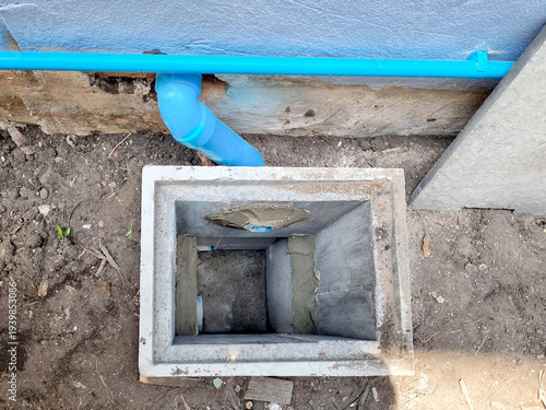 Concrete drainage manhole installation in the ground with blue PVC pipes connected. Square precast concrete pit for sewer system or water management during residential house construction.
