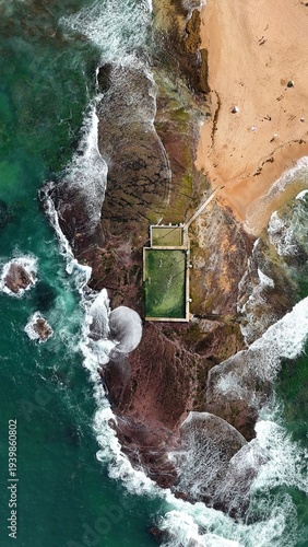 Drone shot aerial view of a beach rock pool and waves crashing over rocks at a beach in Sydney Australia in Summer 