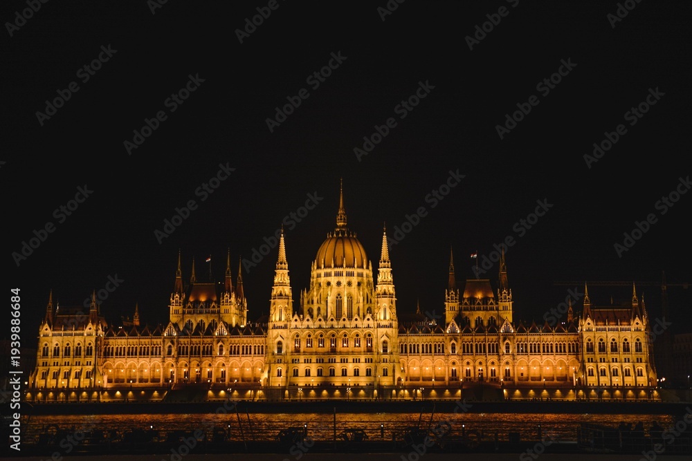 Obraz premium The illuminated Hungarian Parliament Building stands as a majestic landmark over the Danube river at night, reflecting the historic architecture of Budapest, Hungary’s capital city in Europe