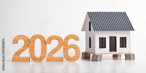 Miniature house raised on stacks of coins and wooden 2026 numbers. Property investment trends, housing market outlook, real estate growth, mortgage planning, and financial goals for the year 2026.