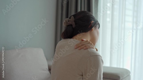 Woman suffering from neck pain while sitting on the couch at home, Health care and medical concept