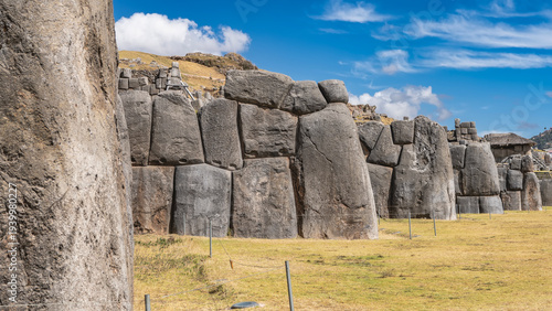 Ruins of the ancient Inca fortress Sacsayhuaman. A jagged wall of huge boulders. The stones are smoothly hewn and closely fitted. Ashlar polygonal masonry. Inca stone architecture. Blue sky, clouds.

