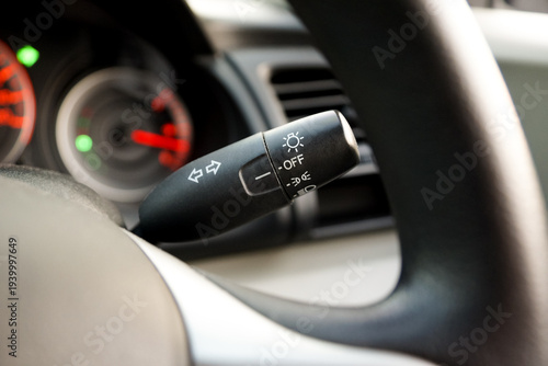 Close-up of a car turn signal and headlight control stalk behind the steering wheel, showing lighting and indicator controls used for vehicle operation and road safety.