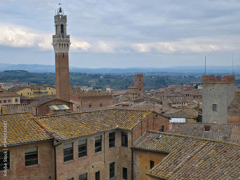 Fototapeta premium Panoramic view of Siena city center with Torre del Mangia tower, historic rooftops and the rolling hills of Tuscany in the background, Italy