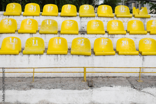 Photos Front view of old yellow plastic seats on weathered concrete stadium tribunes