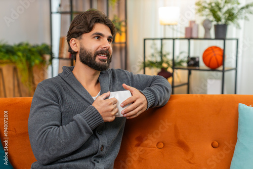Canvas Print Indian man at home holds hot tea or coffee warms hands looks out window gentle smile calm