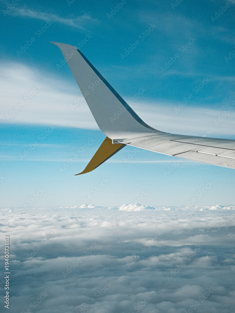 Fototapeta premium Airplane wing above clouds during flight with blue sky aerial travel perspective