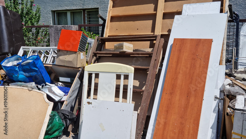 A large pile of discarded wooden boards and old household furniture sits outdoors on a sidewalk ready for disposal and recycling