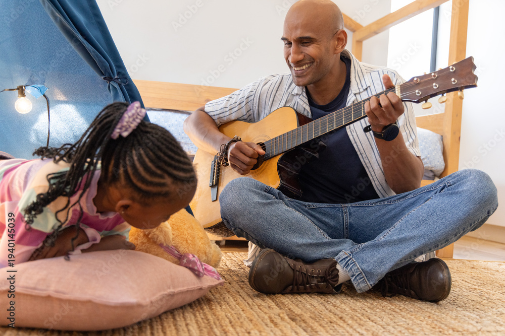 Fototapeta premium African American father and child playing guitar in bedroom, daughter holding teddy
