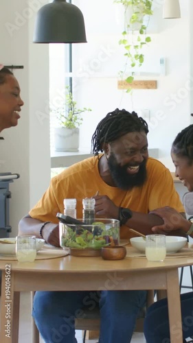 African American family leaning and laughing after man's joke while sharing salad at dining table