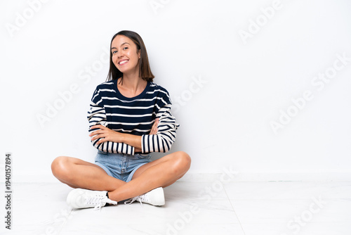 Young caucasian woman sitting on the floor isolated on white background with arms crossed and looking forward