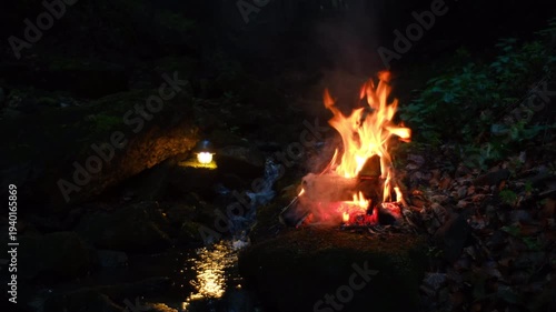Night cozy campfire and small stream in light of flashlight. Calm bonfire, burning old wood in summer time. Active lifestyle, traveling, hiking. Camping vibes and outdoor lifestyle mood