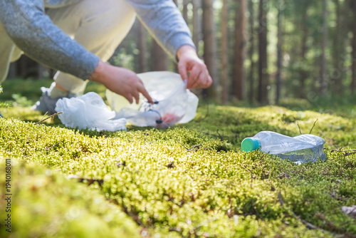 Depersonalized view of person gathering plastic waste in forest. Environmental cleanup activity promoting sustainability and protection of natural ecosystems.