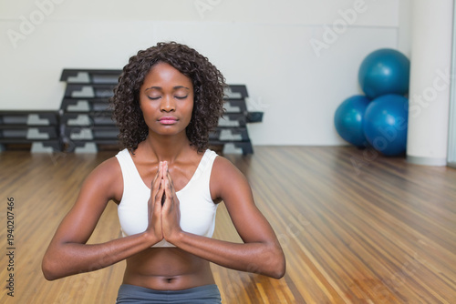 African American woman meditating on gym floor in sports bra and leggings near blue stability balls