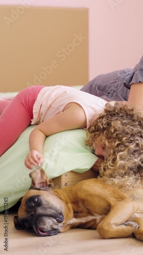 Affectionate little girl with curly hair lying down and petting her beloved boxer dog. Cute child enjoying time with her canine best friend at home