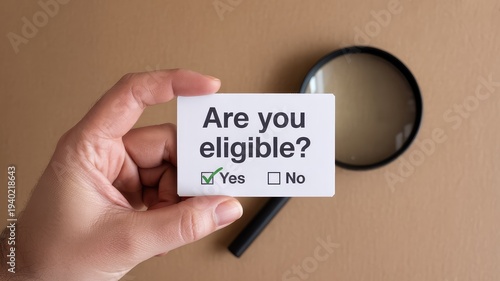 Person holding up a small card asking are you eligible with a magnifying glass nearby on desk