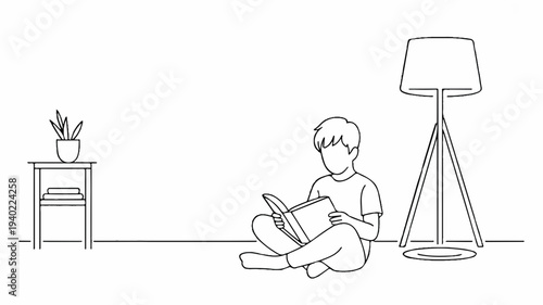 A young boy sits cross legged on floor reading book next to standing lamp and side table with plant