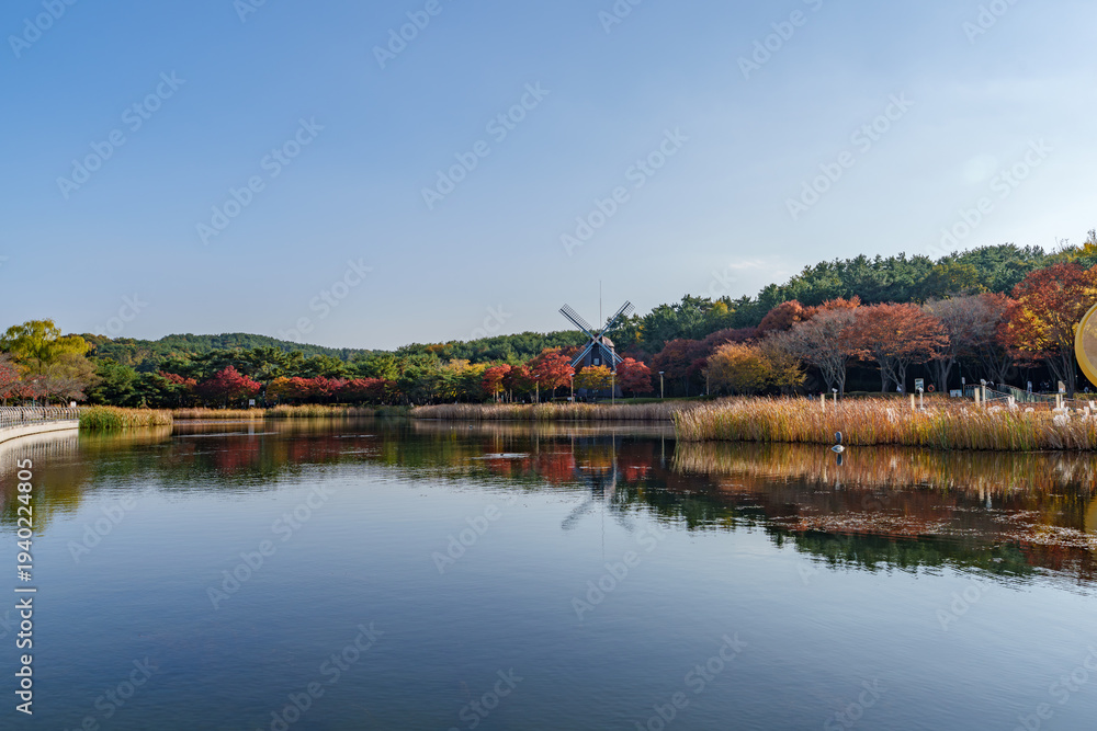 Obraz premium Autumn landscape of Ulsan Grand Park with a windmill and lake reflection, South Korea