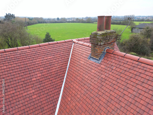 Inspection drone view of a newly installed ceramic roof on an old English farmhouse. The old, brick built chimney stack is visible.