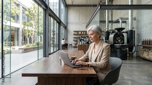 Elegant Senior Woman Executive Working on Laptop in Modern Glass Cafe