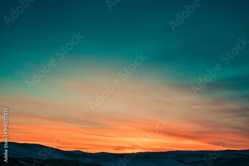 Beautiful sunset over snow covered mountain peaks with teal and orange sky