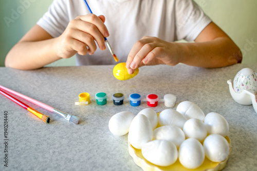 Child painting a yellow Easter egg at home, creative spring craft