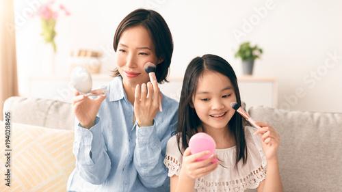 Fotografie A mother and daughter spend time together on a sofa, using makeup brushes and mirrors