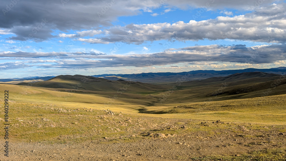 Obraz premium Vast Rolling Steppe Landscape in Mongolia Under Dramatic Cloud Sky at Sunset