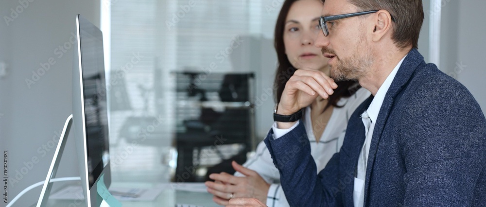 Fototapeta premium Colleagues collaborating, man pointing at desktop computer screen, woman listening during business discussion in office. Businesspeople concept