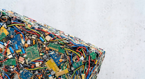 Fotografie Compressed block of recycled e-waste with shredded circuit boards and colorful wires on a light concrete background with copy space