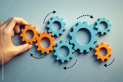 Hand places a small orange gear into a complex system of interconnected blue and orange cogs to demonstrate teamwork and the smooth operation of a productive business unit.