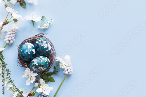 Easter flat lay. Stylish easter eggs in nest and cherry flowers on blue background. Easter celebration, season greetings mockup. Spring modern floral banner