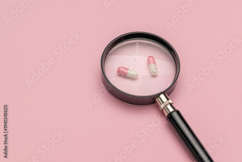 Magnifying Glass Over Capsules on Pink Background: Focus on Medicine and Healthcare Concepts in Stock Photography
