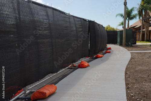 Photography Curved concrete sidewalk winds through a fenced construction site bordered by bl