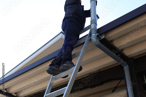 Man on a ladder inspecting home roof and gutters