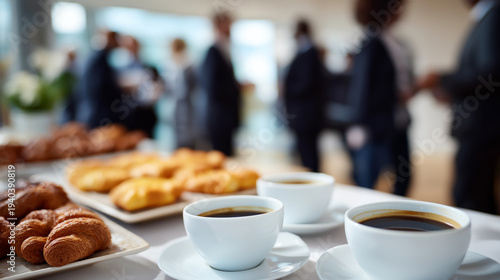 Coffee cups and fresh pastries on a table during a business networking event with people in the background.